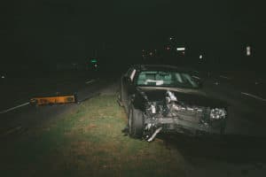 Wrecked car sitting in median and roadway at night next to damaged street light